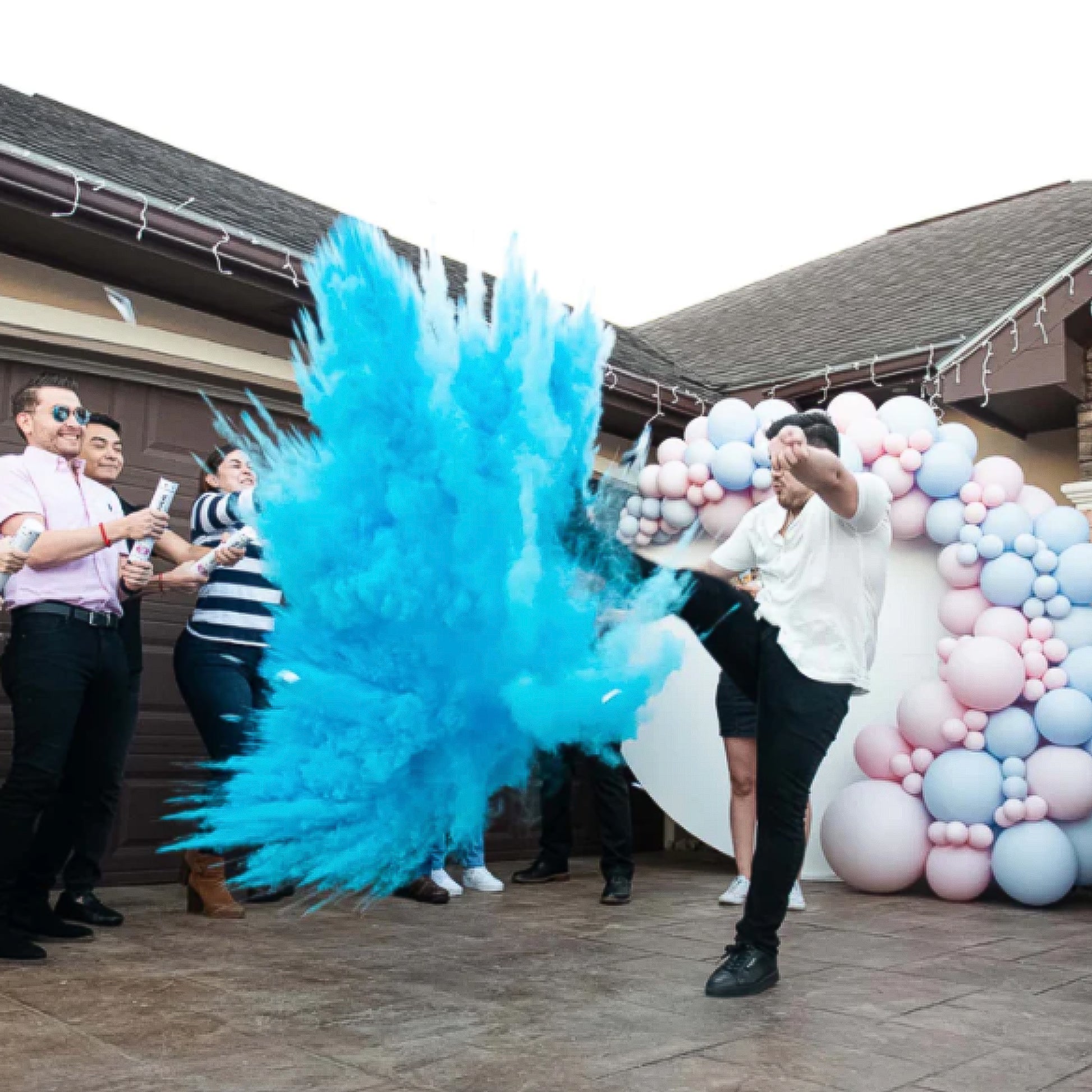 A group celebrating with a Sports Gender Reveal NFL Ball, creating a dramatic explosion of bright blue powder against a backdrop of pink and blue balloon decorations on a patio, capturing the exciting reveal moment.