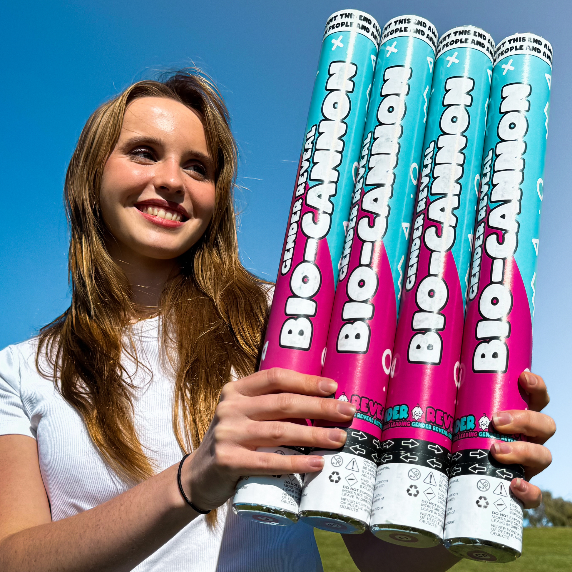 Four XL Bio-Cannon gender reveal confetti and powder cannons in bright pink and blue colors, displayed outdoors against a clear blue sky. Features biodegradable party supplies for gender reveal celebrations and special announcements.