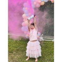 Young girl releasing pink powder from a gender reveal mini extinguisher in front of balloon decorations outdoors