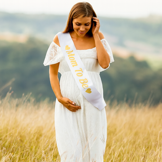 Satin "Mom To Be" Gender Reveal Sash worn by pregnant woman in white dress outdoors in field.