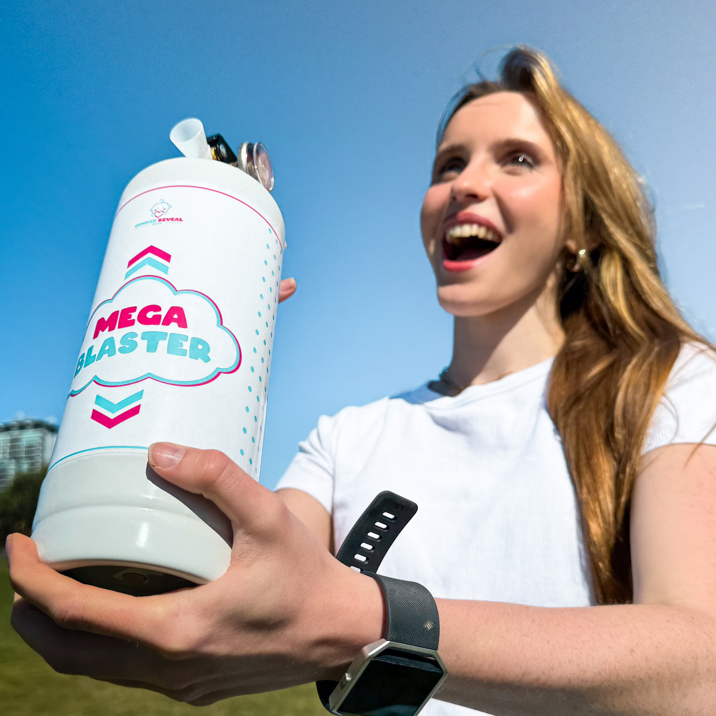 MEGA Blaster Gender Reveal Extinguisher shown outdoors against blue sky, featuring white canister with pink and blue logo design, held by someone wearing a white t-shirt and smartwatch on a sunny day