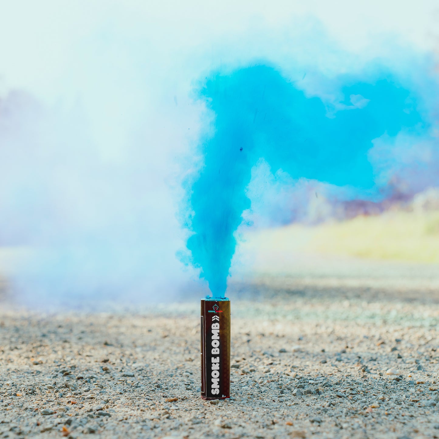 Extreme Gender Reveal Smoke Bomb emitting vibrant blue smoke against a soft sky background, standing upright on rocky ground, demonstrating the product's powerful colored smoke effect for gender reveal celebrations.