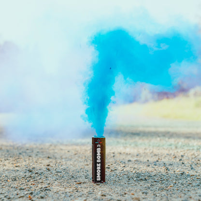 Extreme Gender Reveal Smoke Bomb emitting vibrant blue smoke against a soft sky background, standing upright on rocky ground, demonstrating the product's powerful colored smoke effect for gender reveal celebrations.